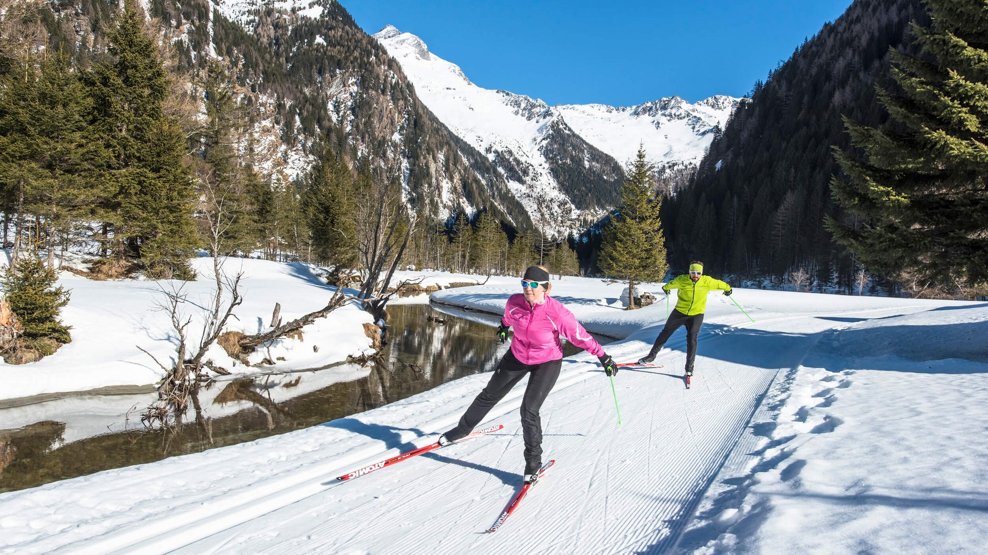 Zwei Langläufer beim Ski fahren im verschneiten Gebirgstal bei Sonnenschein
