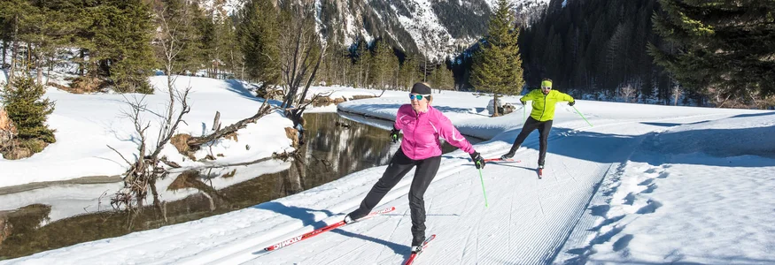 Zwei Langläufer beim Ski fahren im verschneiten Gebirgstal bei Sonnenschein