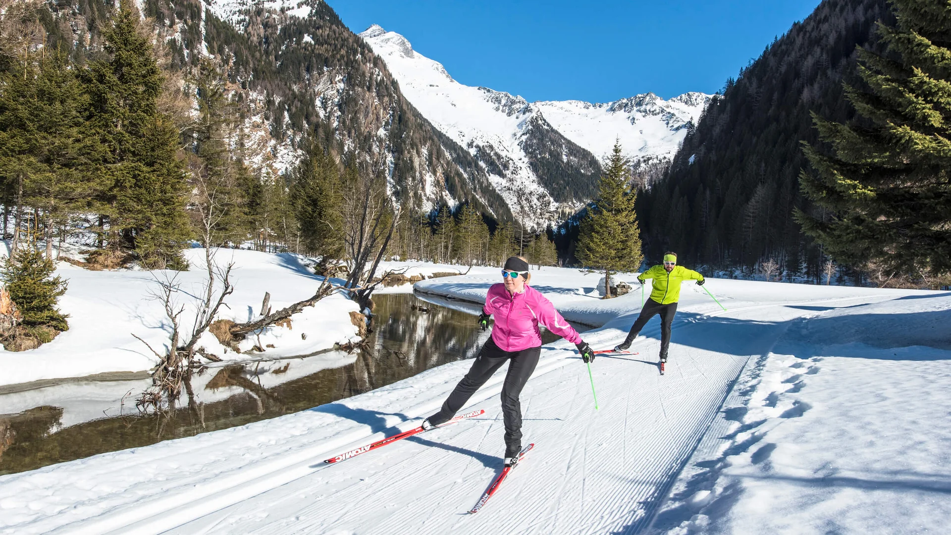 Zwei Langläufer beim Ski fahren im verschneiten Gebirgstal bei Sonnenschein