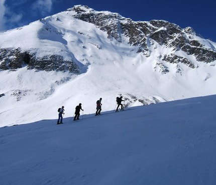 Vier Wanderer steigen im Schnee vor schneebedecktem Berg unter blauem Himmel auf