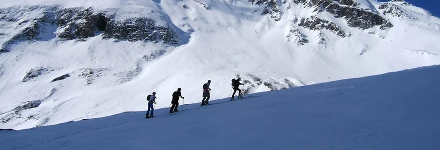 Vier Wanderer steigen im Schnee vor schneebedecktem Berg unter blauem Himmel auf