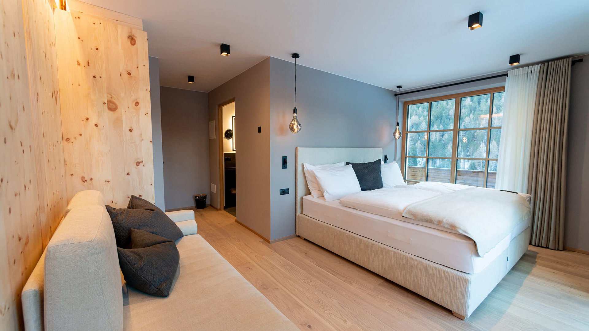 Modernes Schlafzimmer mit Doppelbett, Sofa und großem Fenster mit Bergblick