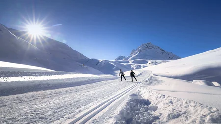Zwei Skifahrer auf einer sonnigen, verschneiten Bergloipe