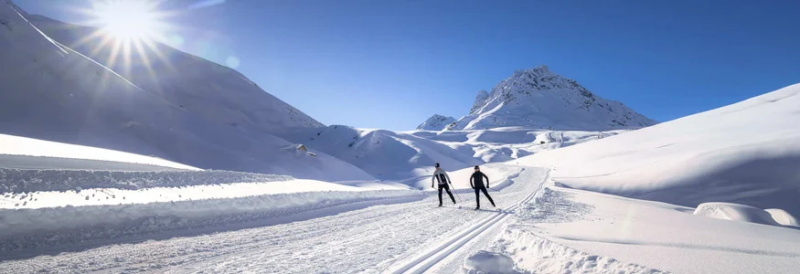Zwei Skifahrer auf einer sonnigen, verschneiten Bergloipe