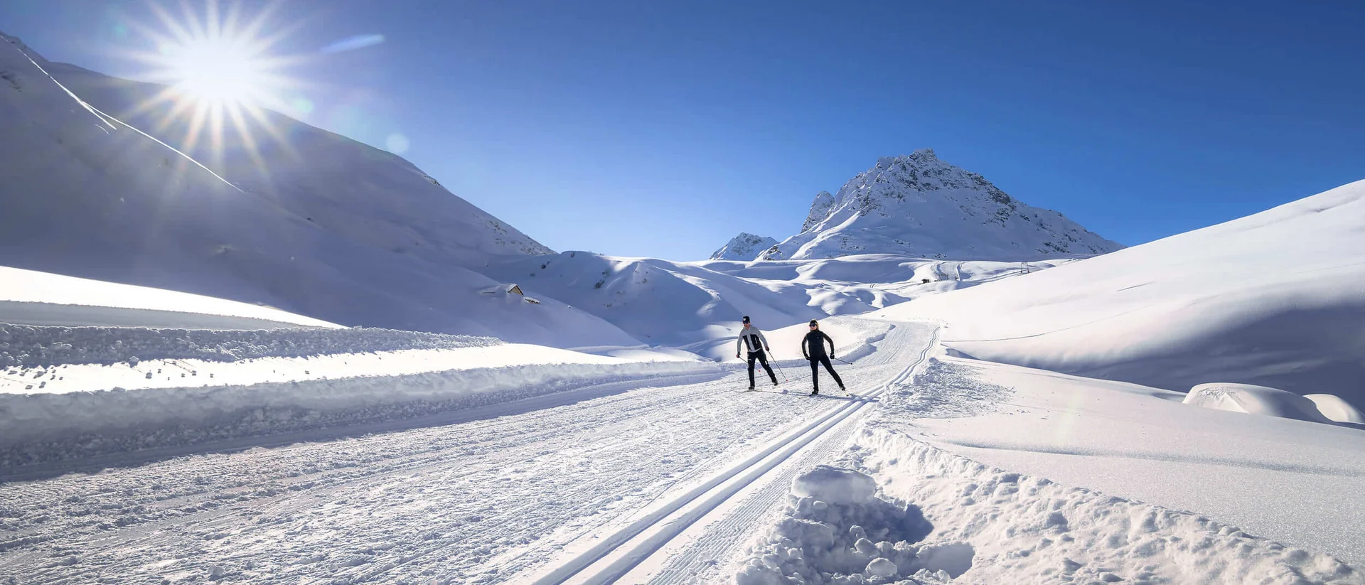 Zwei Skifahrer auf einer sonnigen, verschneiten Bergloipe
