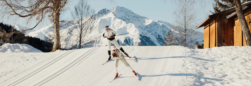 Zwei Langläufer fahren im Winter bei Bergkulisse auf Schnee