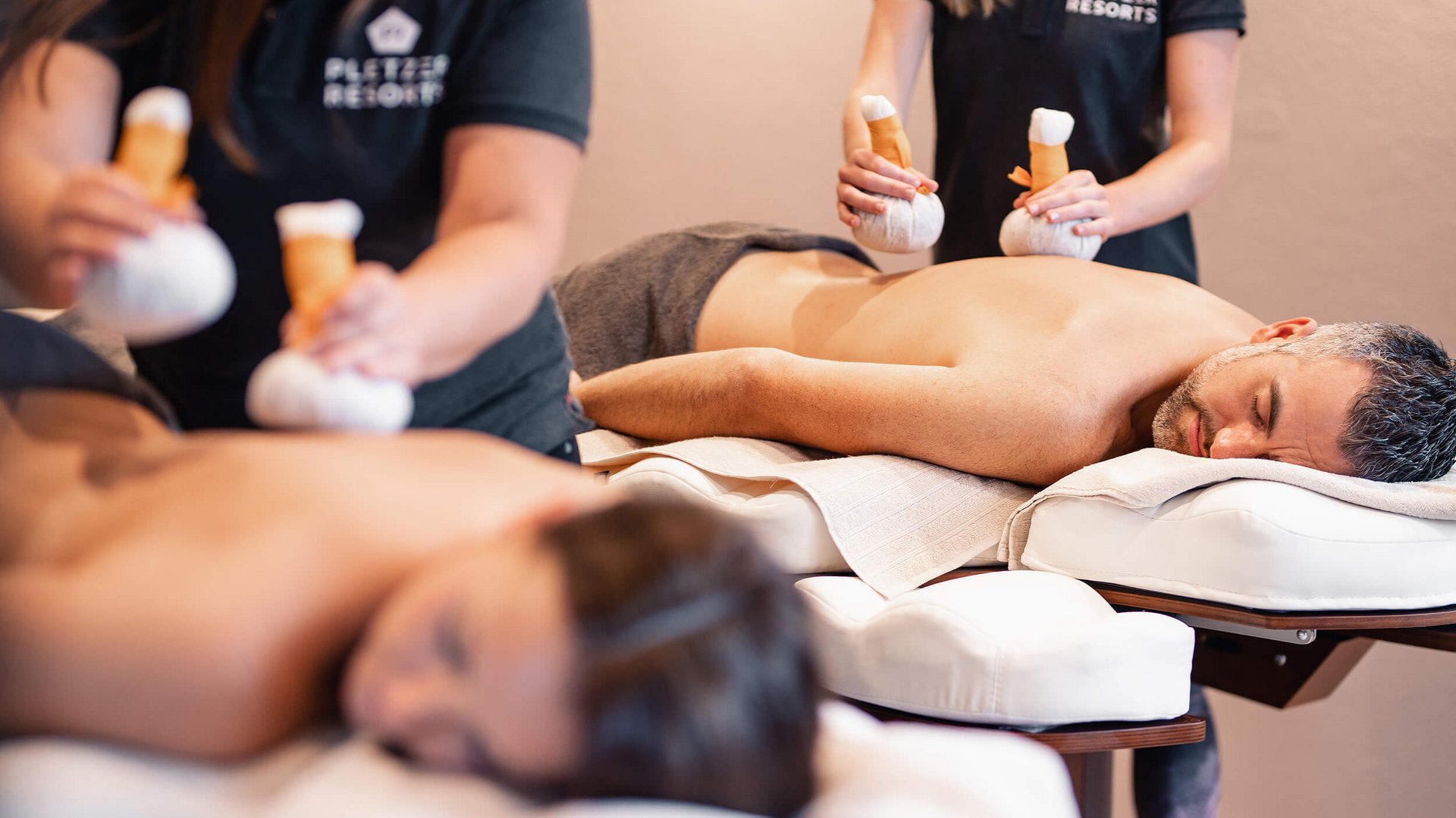 Two people receiving herbal compress massage at a spa