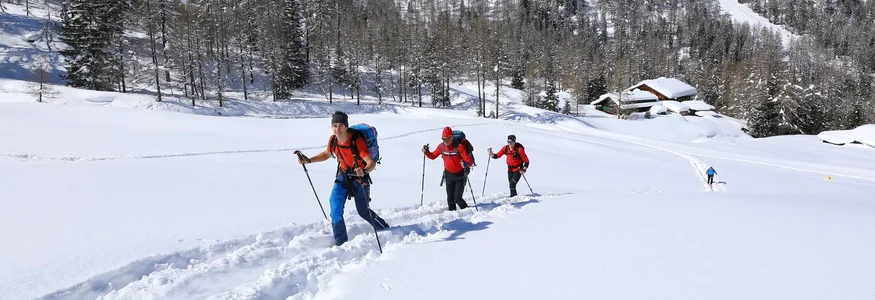Drei Wanderer stapfen bei sonnigem Wetter durch tiefen Schnee in den Bergen