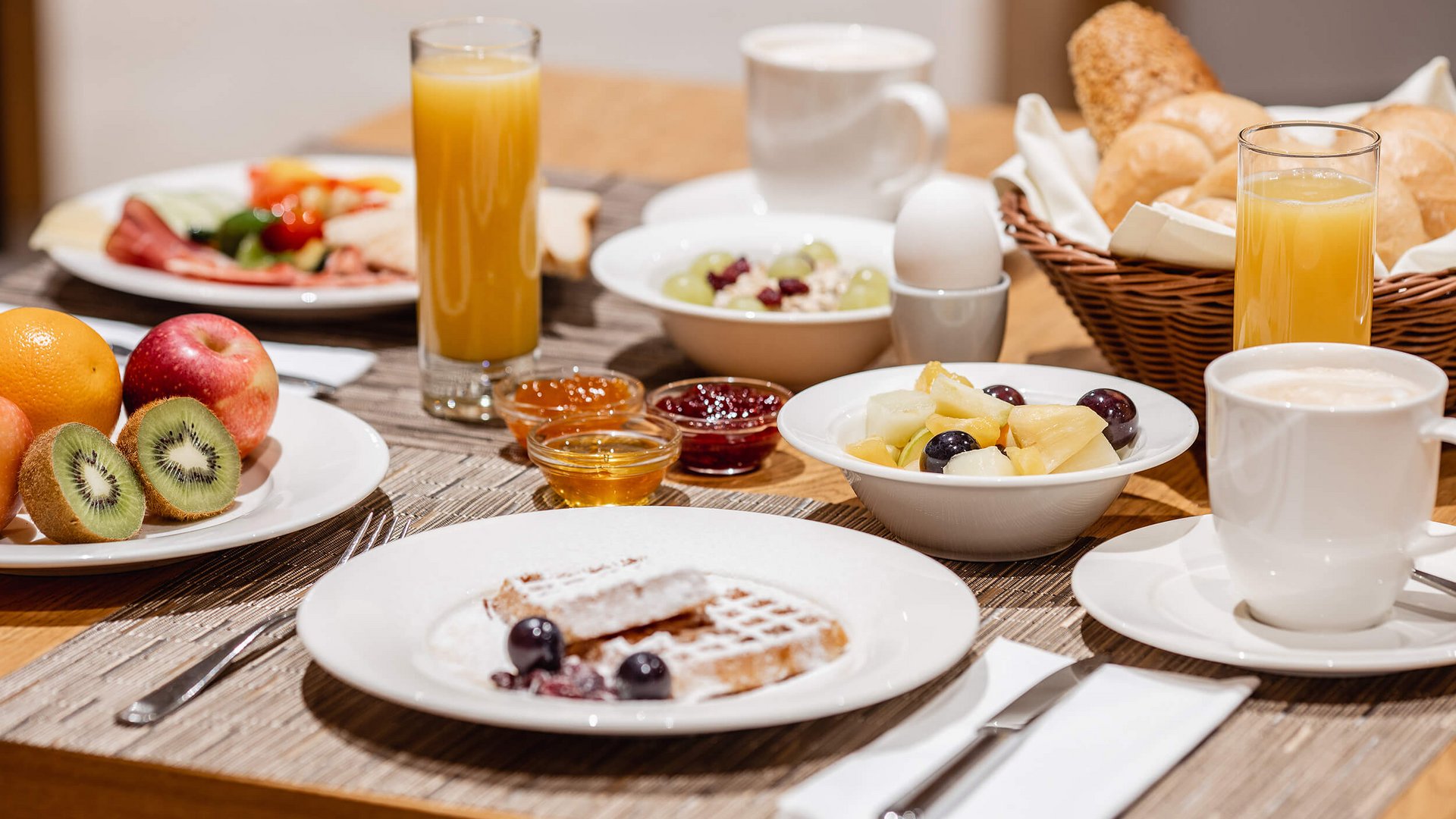 Breakfast table with fruit, waffles, juice, coffee, and rolls