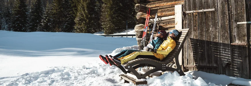 Alpenhotel Karwendel **** © Region Seefeld - Moritz Klee Zwei Personen entspannen auf Liegestühlen neben einer Holzhütte im Schnee