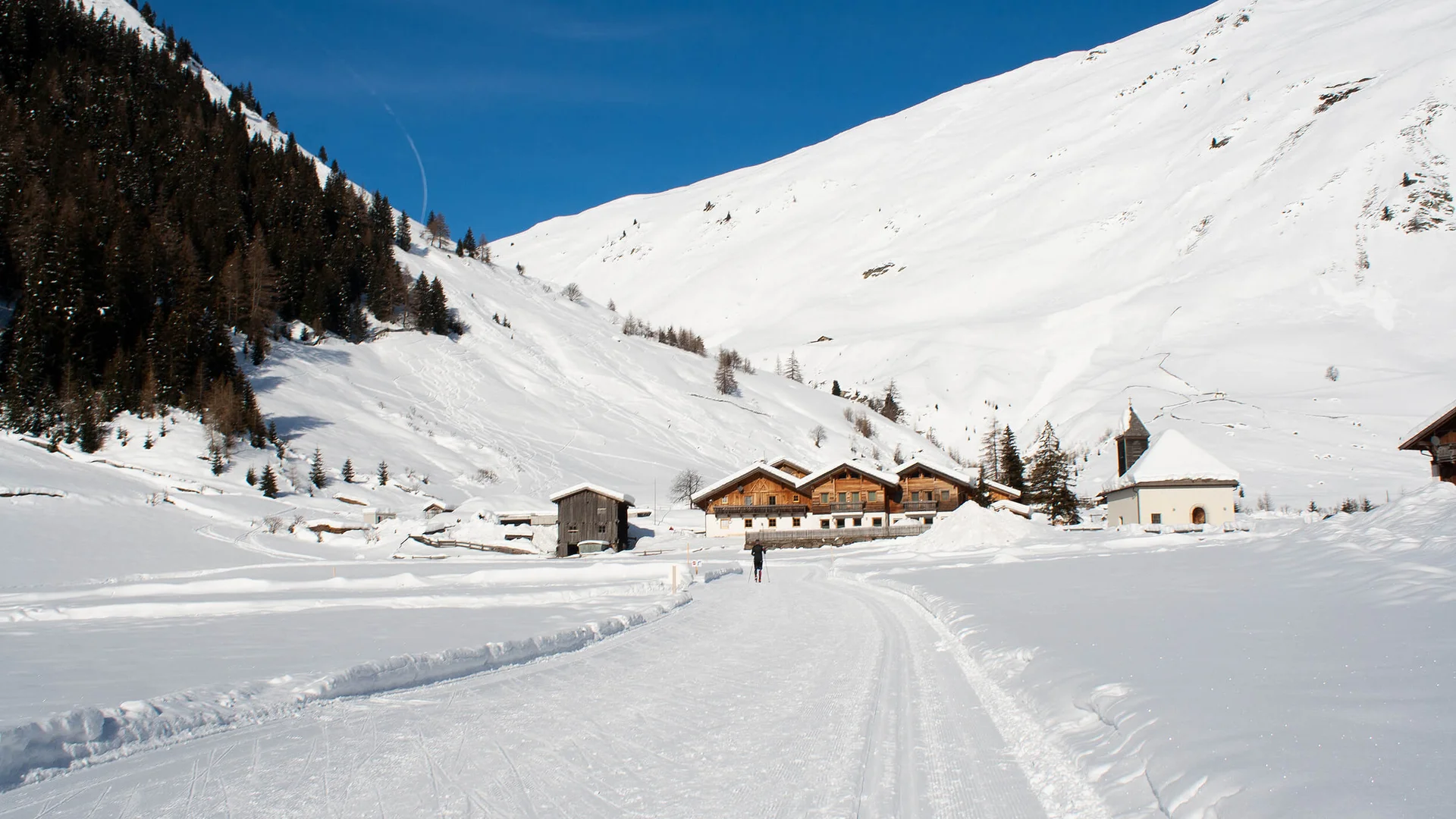 Winterlandschaft mit Schlittenfahrt auf verschneiter Straße und Häusern vor Bergen