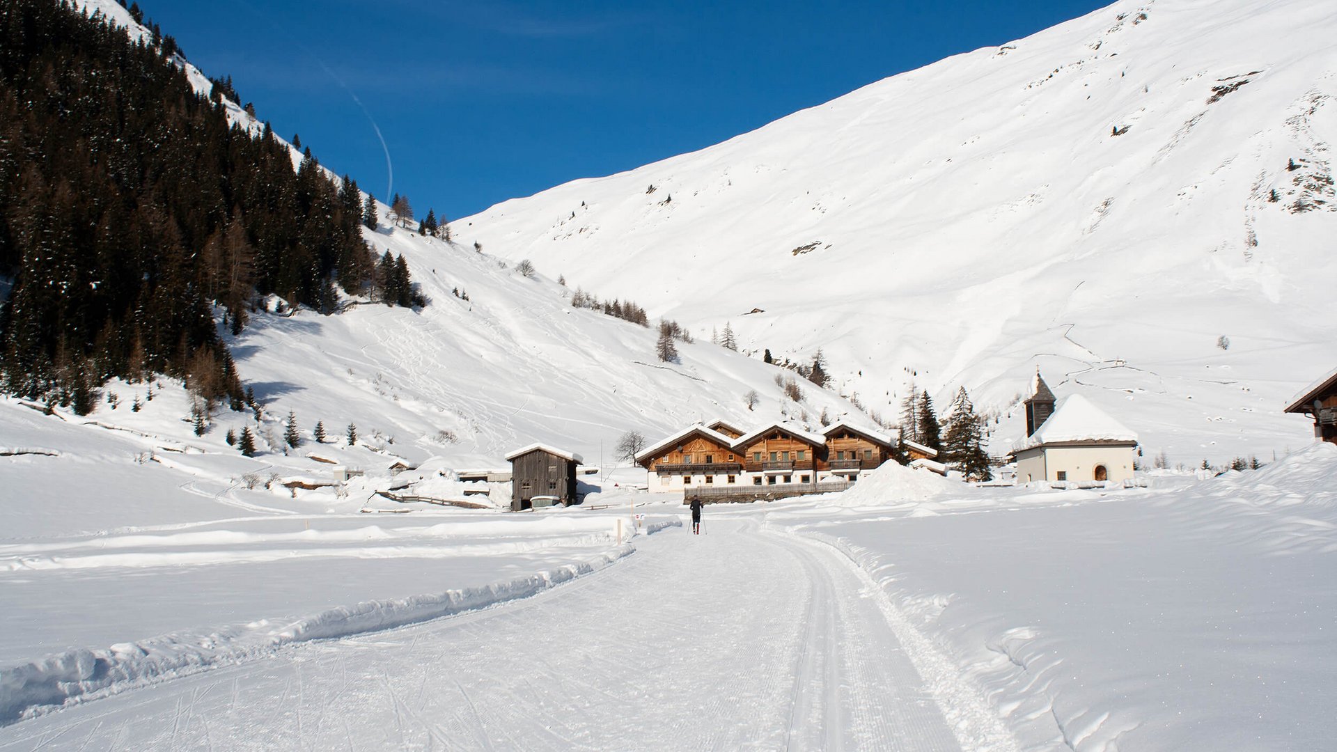 Winterlandschaft mit Schlittenfahrt auf verschneiter Straße und Häusern vor Bergen