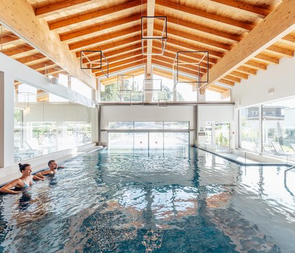 Das Walchsee Aktivresort © Daniel Waschnig Photography Zwei Personen entspannen im Hallenbad mit Holzdecke und großen Fenstern