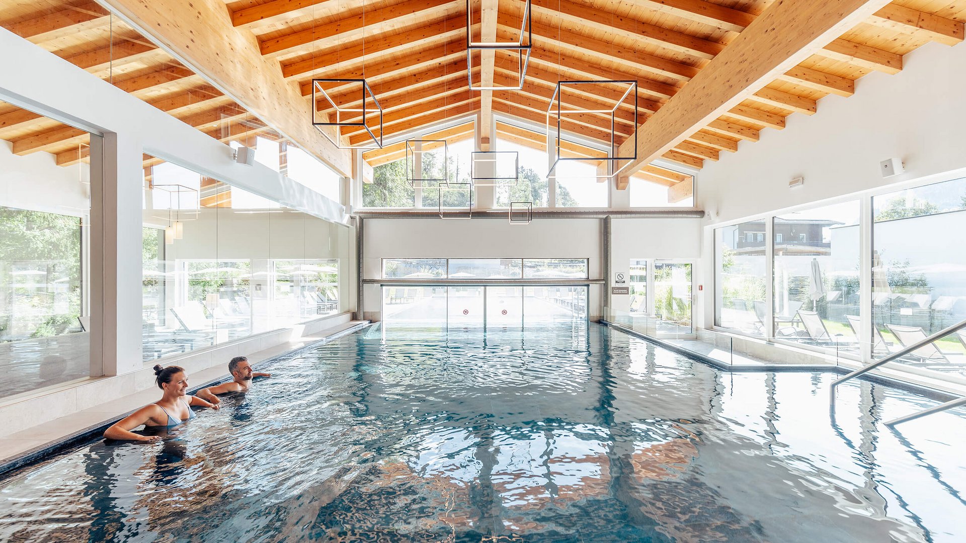 Two people relaxing in indoor pool with wooden ceiling and large windows