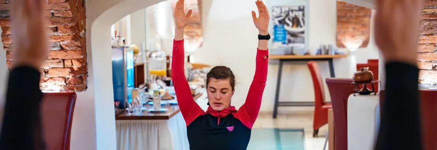 Trainieren im Hotel Loncium © Sportalpen Frau macht Yogaübungen mit erhobenen Armen in Innenraum