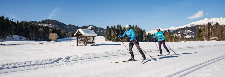 Two people cross-country skiing on a snowy trail in a winter landscape