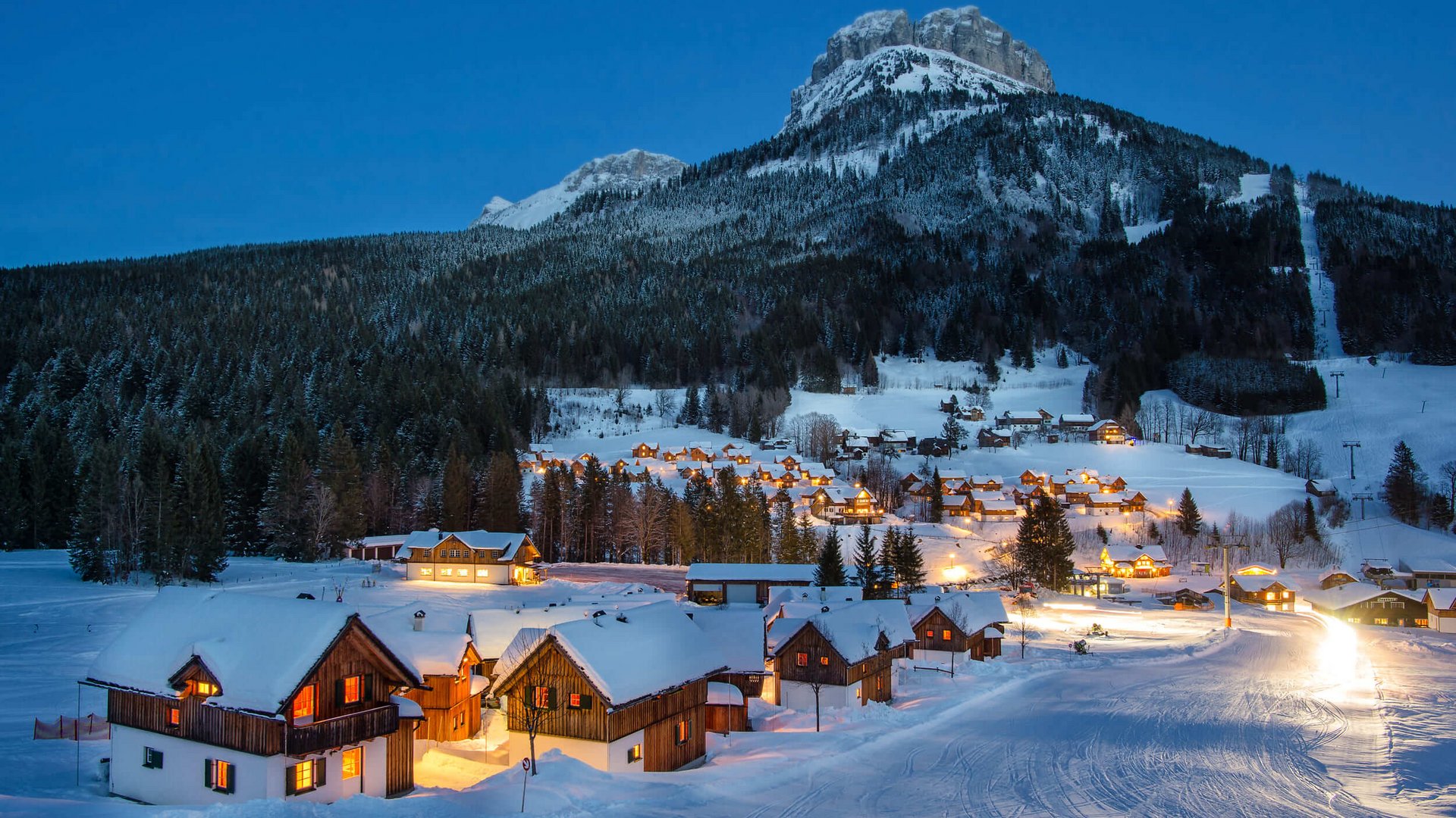 Snow-covered village with lit houses and forested mountains at night