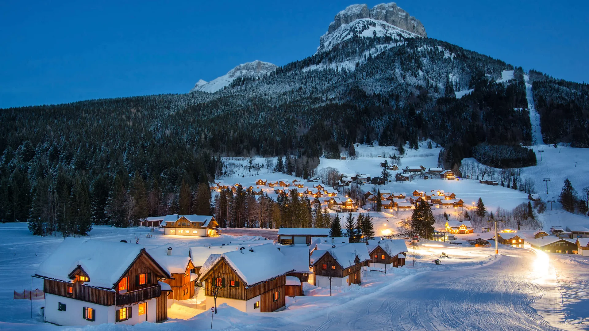 Snow-covered village with lit houses and forested mountains at night