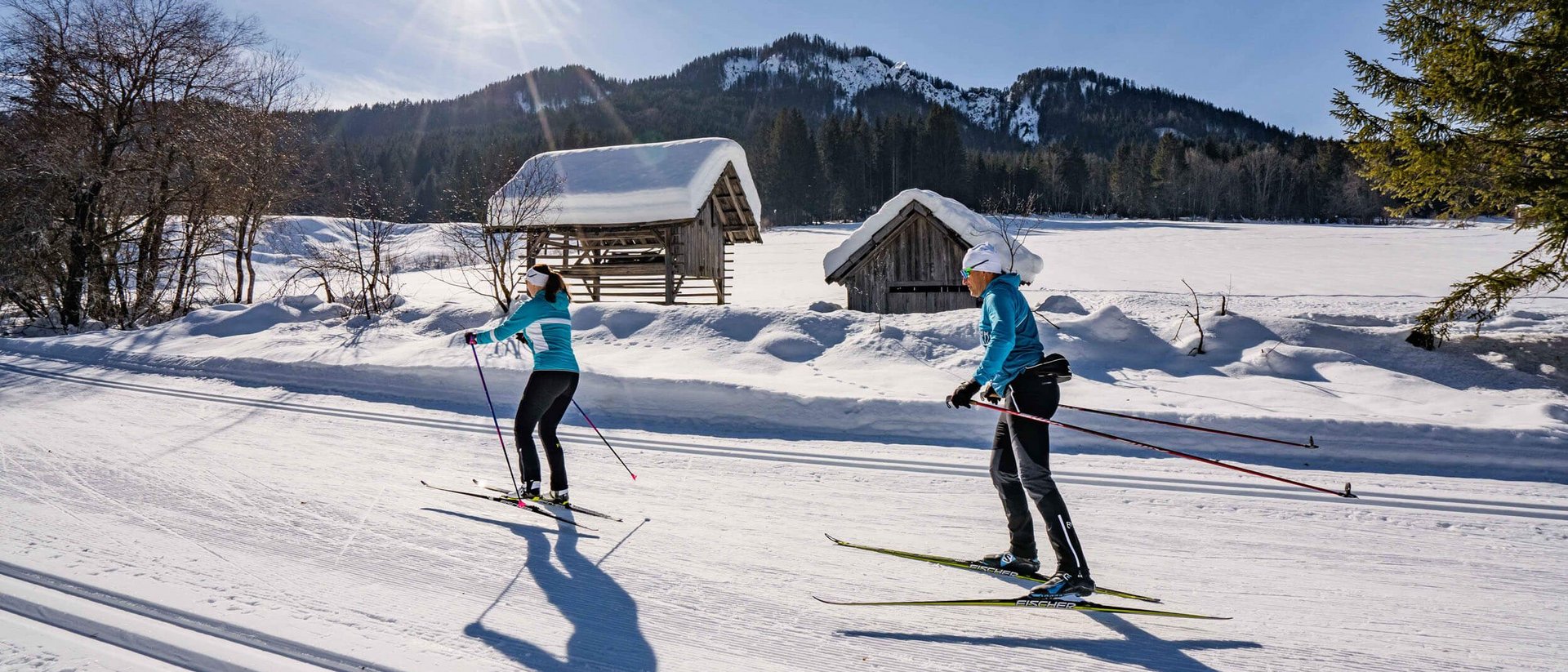 Zwei Langläufer bei sonnigem Winterwetter auf verschneiter Loipe