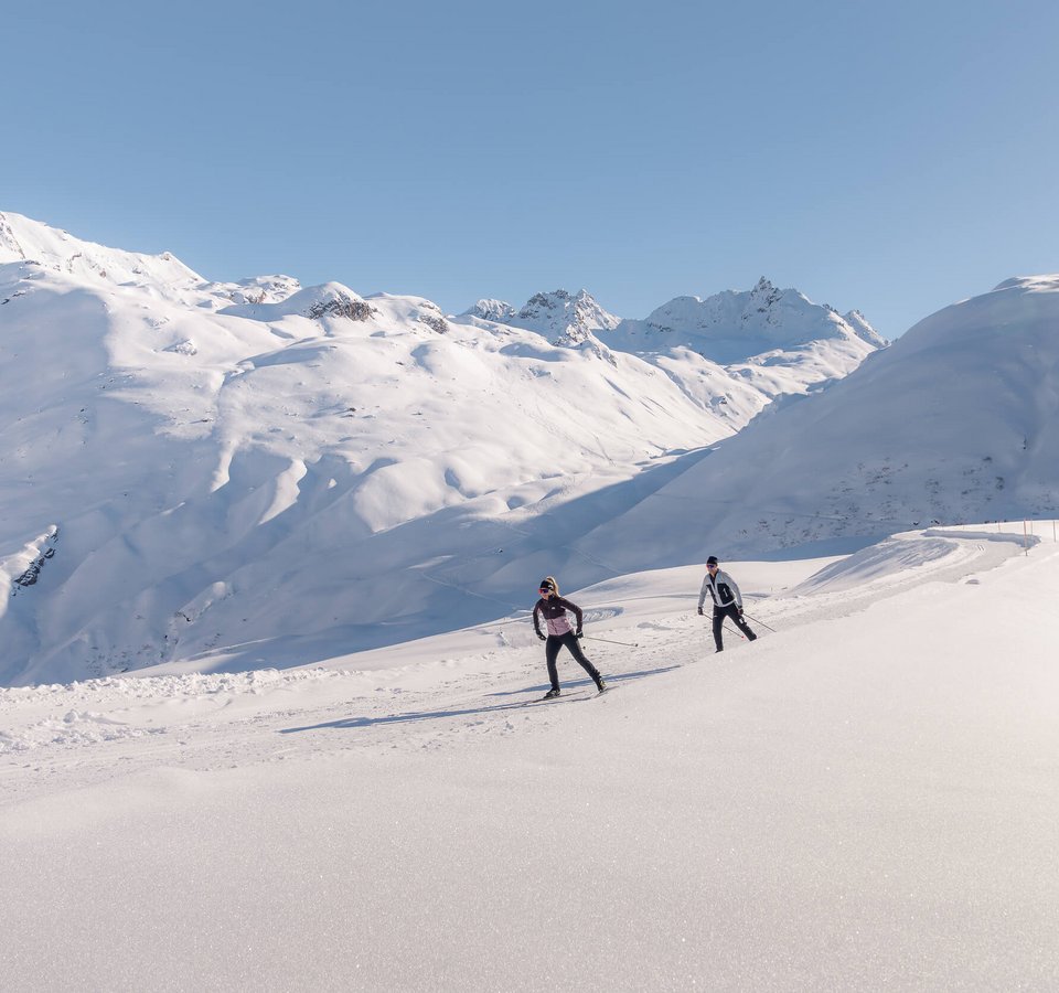 Höher geht’s nicht – Gletscher- & Höhenloipen © TVB Paznaun-Ischgl Zwei Langläufer auf verschneiter Berglandschaft bei klarem Himmel