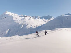 Two cross-country skiers in snowy mountain landscape under clear sky