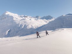 Two cross-country skiers in snowy mountain landscape under clear sky