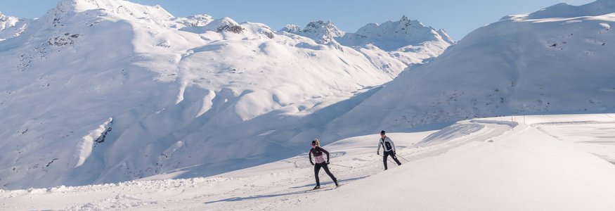 Zwei Langläufer auf verschneiter Berglandschaft bei klarem Himmel