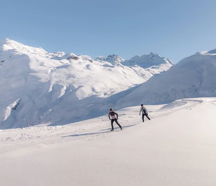 Two cross-country skiers in snowy mountain landscape under clear sky