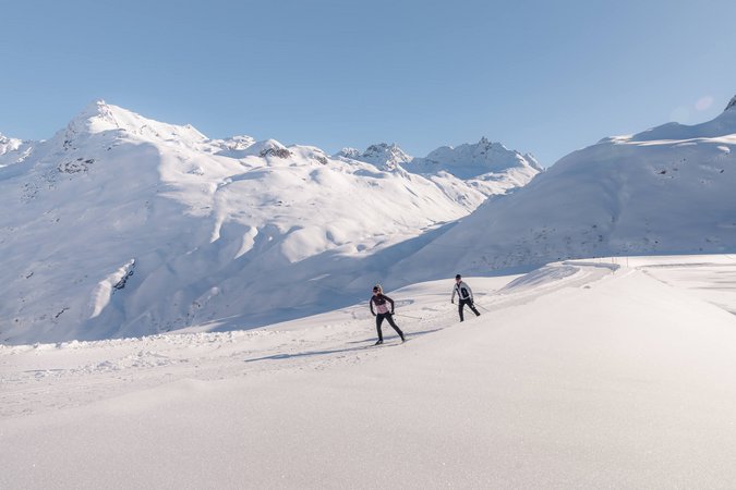 Zwei Langläufer auf verschneiter Berglandschaft bei klarem Himmel