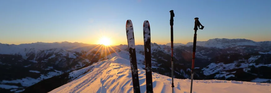 Skier und Skistöcke im Schnee bei Sonnenuntergang in den Bergen