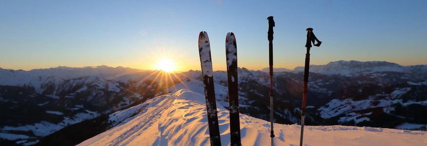 Skier und Skistöcke im Schnee bei Sonnenuntergang in den Bergen