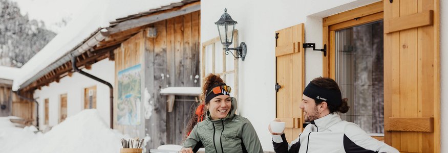 Zwei Personen genießen im Winter warme Getränke vor einem Holzhaus