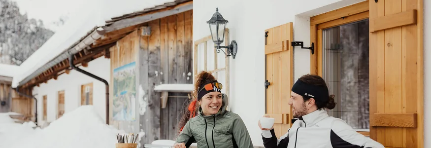 Zwei Personen genießen im Winter warme Getränke vor einem Holzhaus