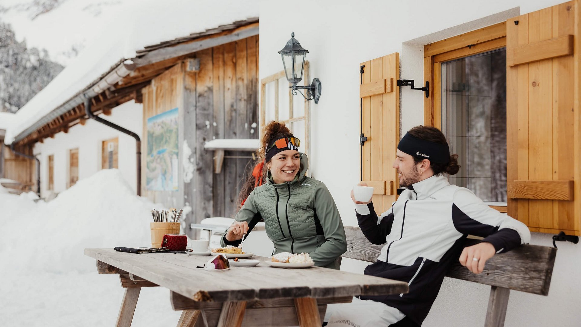 Zwei Personen genießen im Winter warme Getränke vor einem Holzhaus