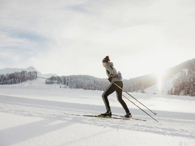 Woman cross-country skiing in snowy winter landscape with sunlight