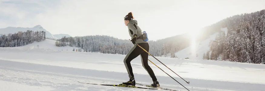 Frau beim Langlaufen auf verschneiter Winterlandschaft bei Sonnenlicht