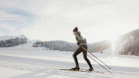 Frau beim Langlaufen auf verschneiter Winterlandschaft bei Sonnenlicht