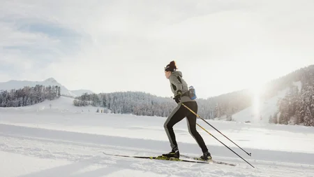 Woman cross-country skiing in snowy winter landscape with sunlight