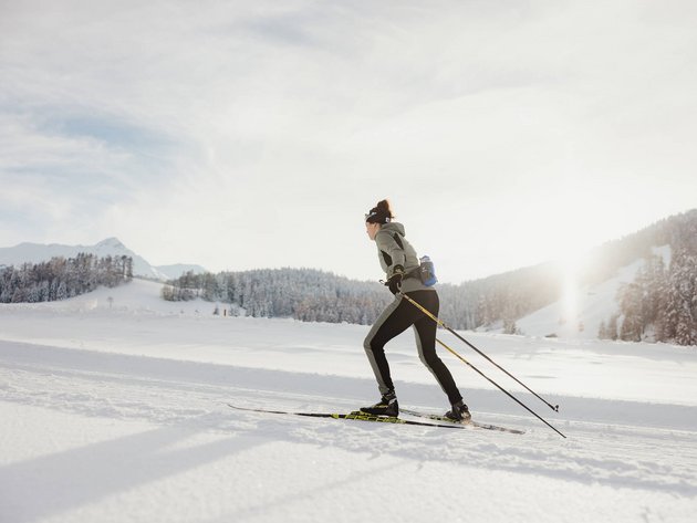 Frau beim Langlaufen auf verschneiter Winterlandschaft bei Sonnenlicht