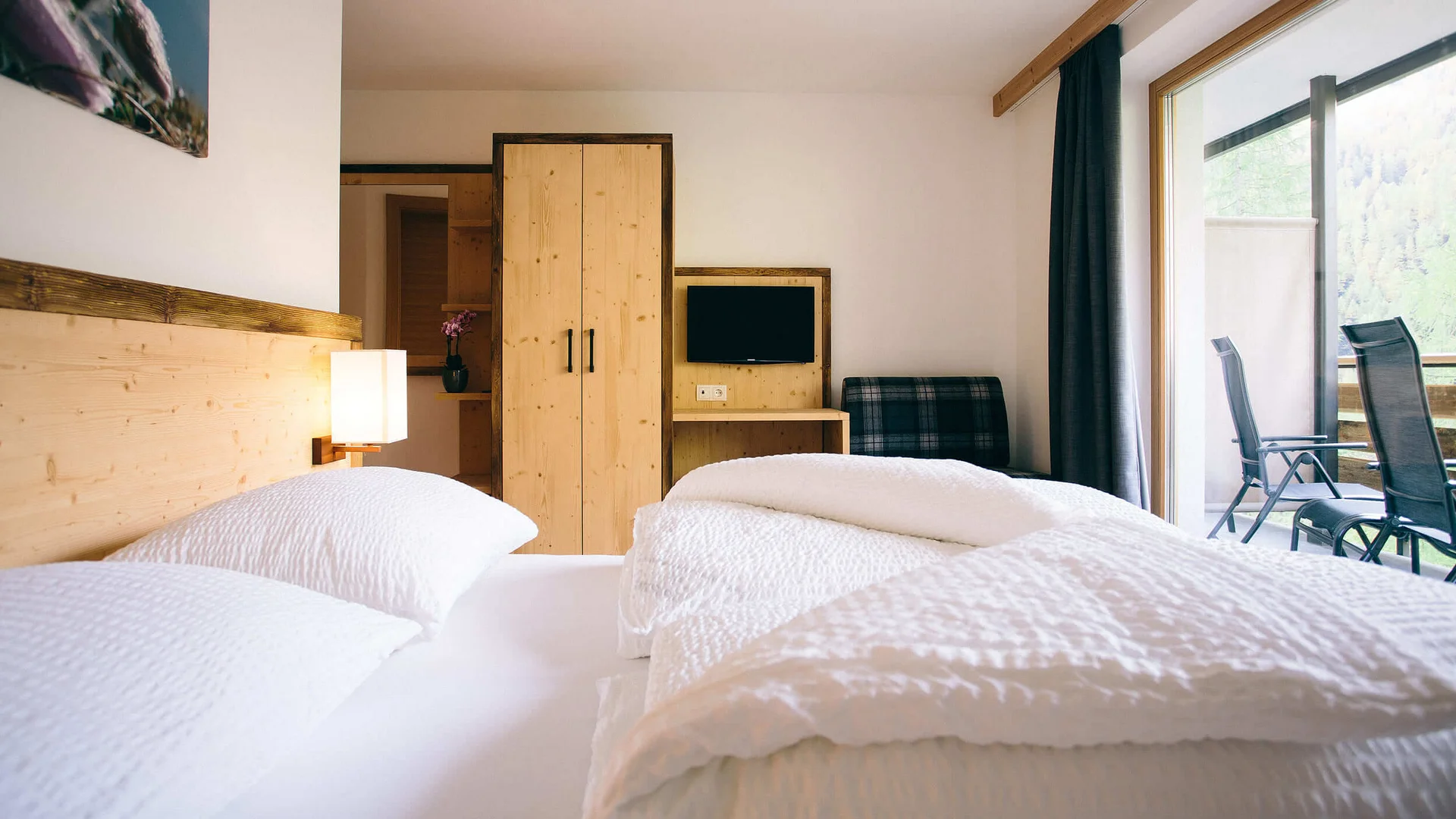 Helles Hotelzimmer mit Doppelbett, Holzmöbeln und Balkon mit Stühlen