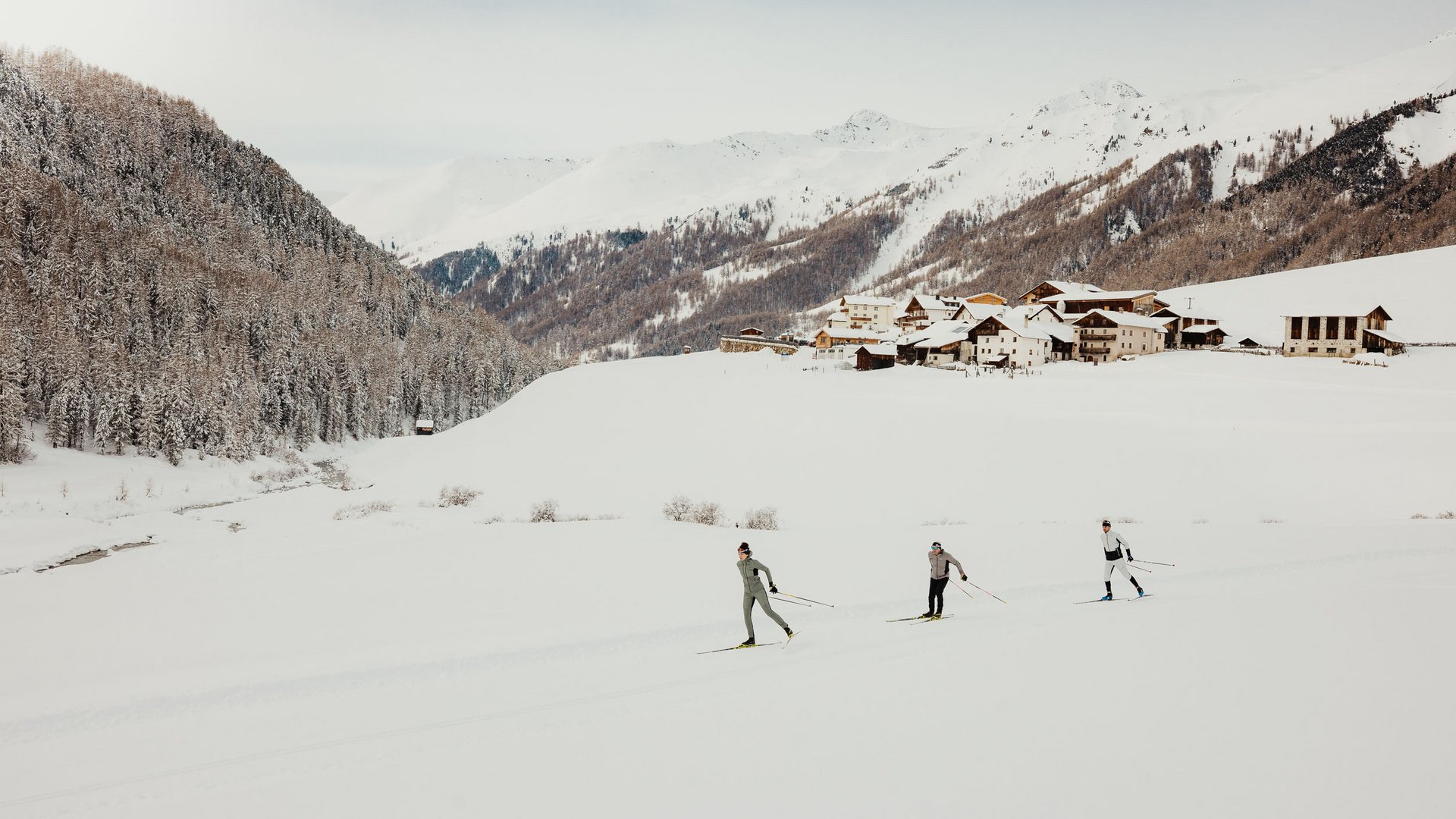 Loipen & Loipenericht © Alex Moling Drei Skilangläufer im Schnee vor verschneitem Dorf und Bergen