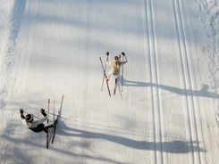 Two people cross-country skiing on a snowy trail seen from above
