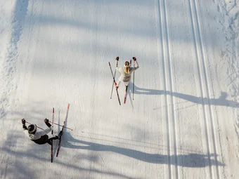 Two people cross-country skiing on a snowy trail seen from above