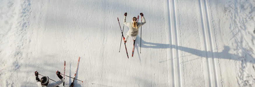Zwei Menschen beim Langlaufen auf verschneiter Loipe von oben gesehen