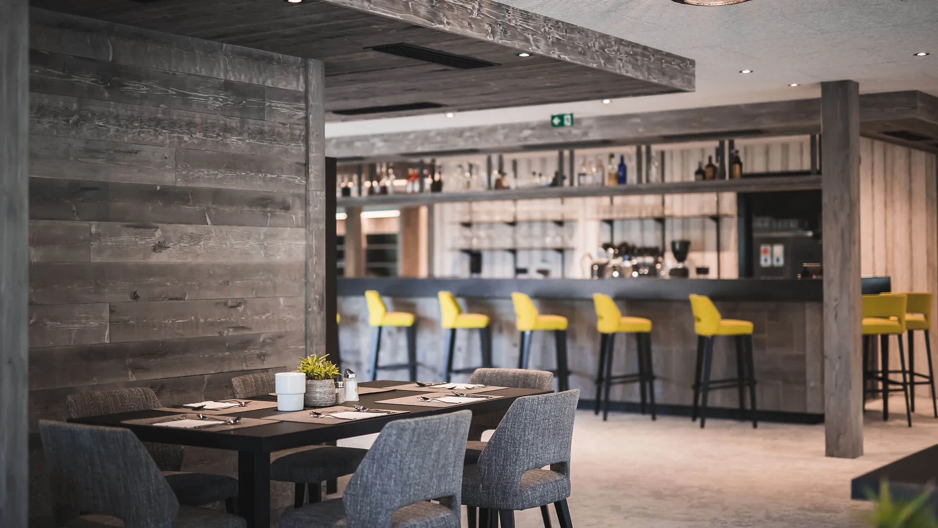 Hirben Naturlaub **** © Manuel Kottersteger Moderner Restaurantbereich mit Holzwänden, grauen Stühlen und gelben Barhockern