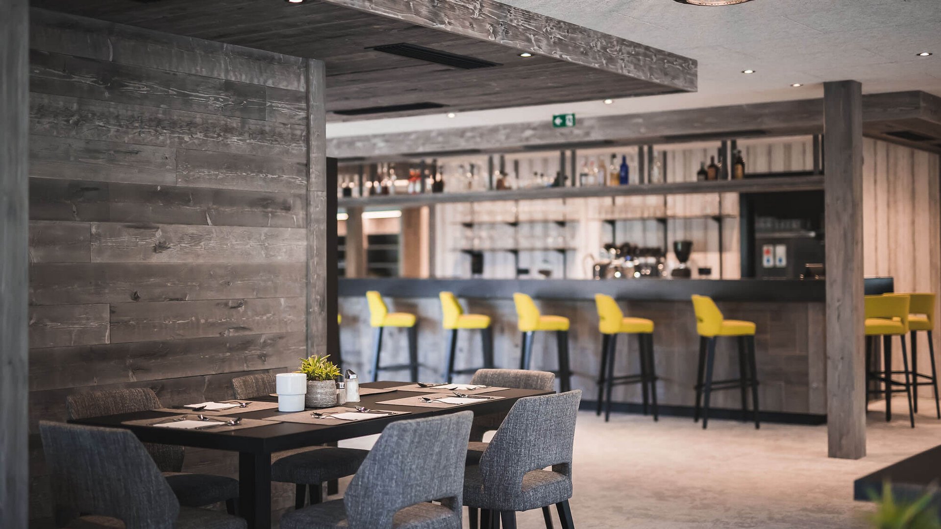 Moderner Restaurantbereich mit Holzwänden, grauen Stühlen und gelben Barhockern