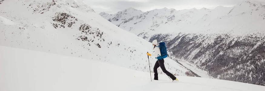 Skier with backpack in snowy mountain landscape under cloudy sky