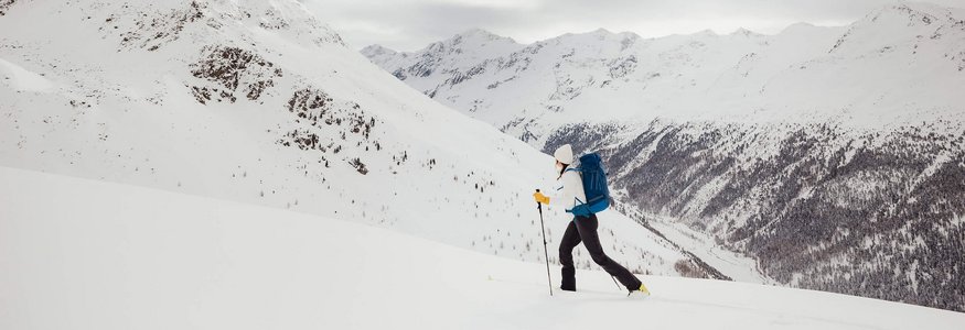 Skifahrer mit Rucksack in verschneiter Berglandschaft bei bewölktem Himmel