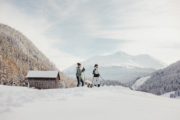 Two people cross-country skiing in snowy mountain valley with huts in background