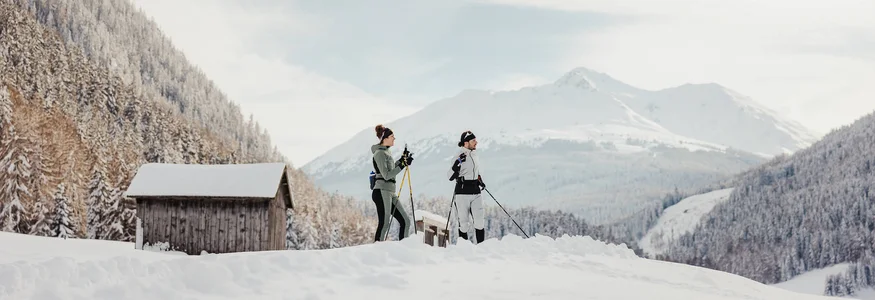 Two people cross-country skiing in snowy mountain valley with huts in background